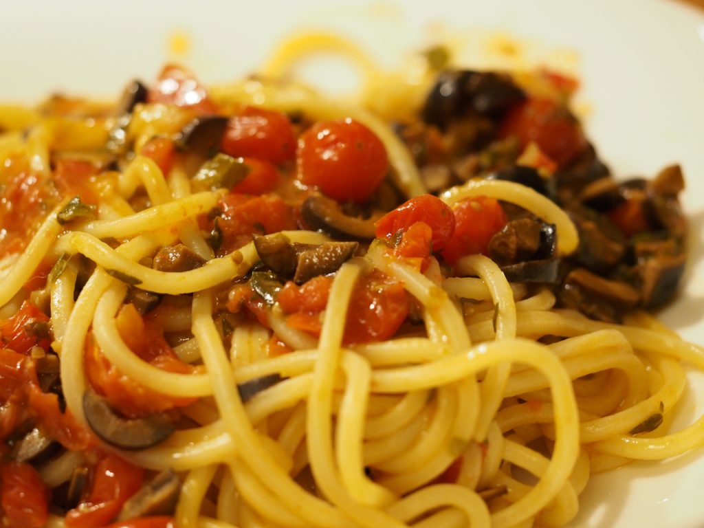 Detailaufnahme einer Portion Spaghetti mit einer Sauce aus Sardelle, Kapern, Oliven, Tomaten und frischen Kräutern
