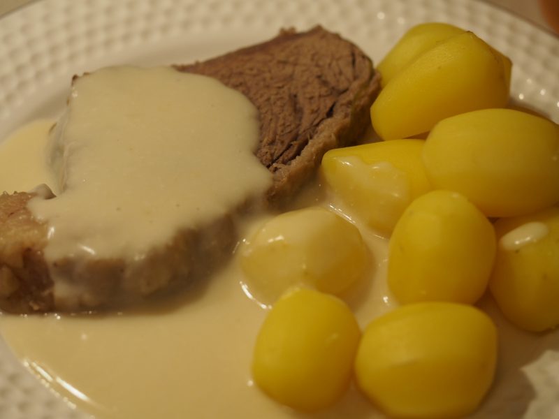 Eine Scheibe des Tafelspitz auf einem Teller zusammen mit gekochten kleinen Kartoffeln und einer Meerrettich Sauce.