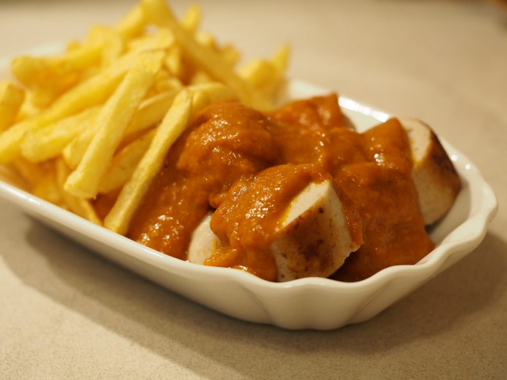 Eine aufgeschnittene Wurst mit Currywurstsauce in einem Schälchen mit Pommes