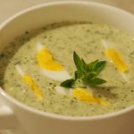 Eine Suppentasse gefüllt mit einer Oregano Suppe mit gevierteltem hart gekochtem Ei