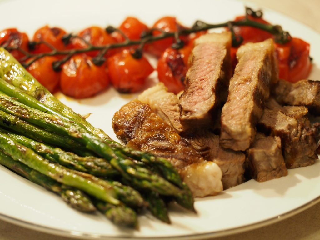 Augeschnittenes gegrilltes Steak neben gegrillten Rispentomaten und grünem Spargel