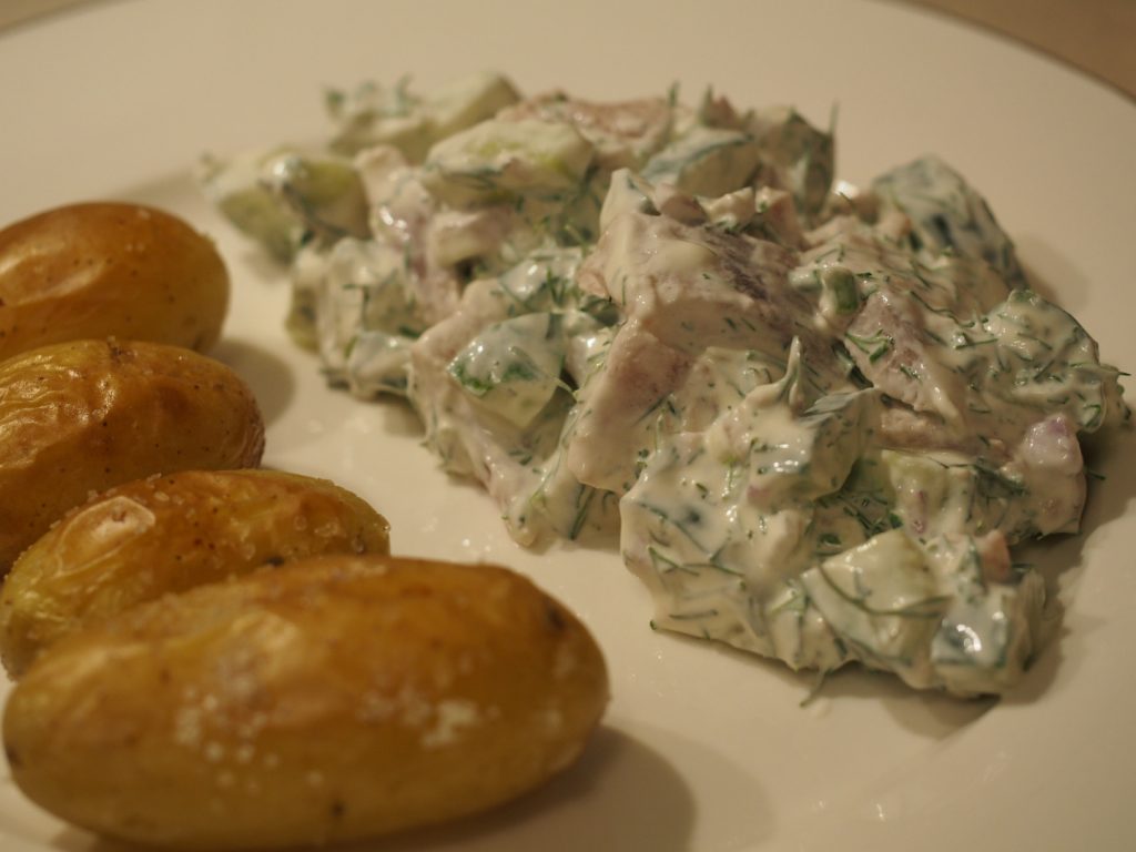 Ein paar Ofenkartoffeln neben etwas Matjessalat mit Gurke, Dill und Schmand.