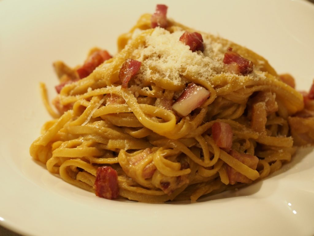 Eine Portion der Miso Carbonara auf einem Pastateller, bestreut mit geriebenen Grana Padano