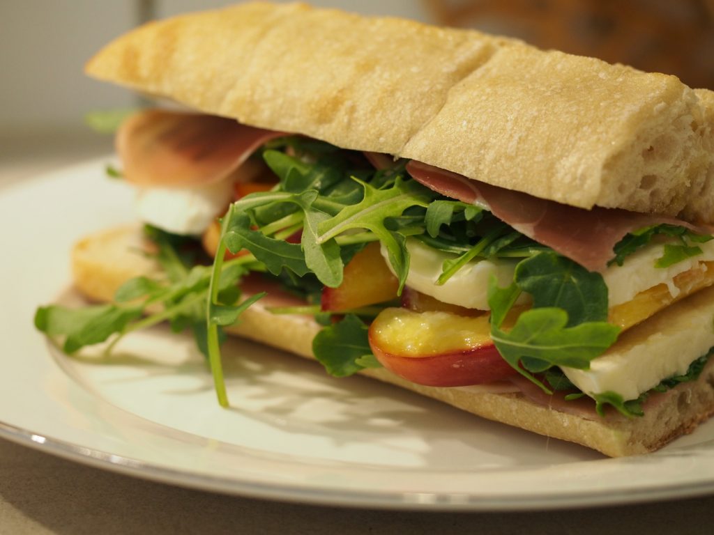 Ein Sandwich aus Ciabatta Brot mit Parmaschinken, Rucola, Mozzarella und Pfirsich oder Nektarine
