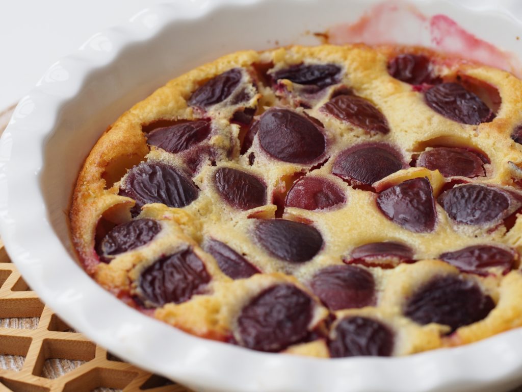 ein französischer Clafoutis mit Zwetschgen in einer runden weißen Auflaufform mit gewelltem Rand