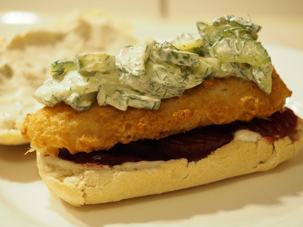 Ein Backfischbrötchen noch ohne die obere Brötchenhälfte mit roter Bete und Gurkensalat