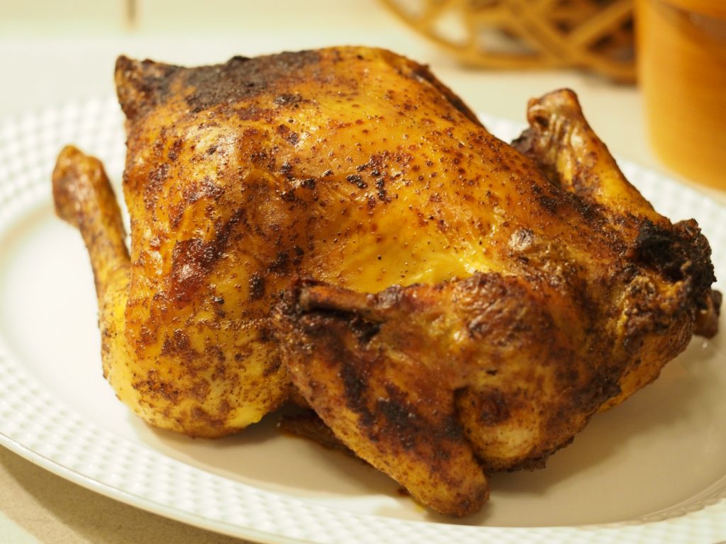 Ein ganzes fertig gebackenes Brathähnchen mit goldgelber crosser Haut, die an manchen Stelle etwas dunkel geworden ist, da wo sich die Gewürze gesammelt hatten.