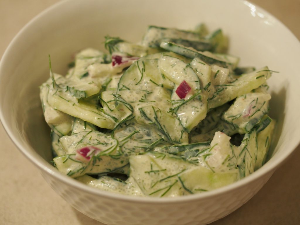 Eine kleine Schüssel gefüllt mit einer Portion vom Gurkensalat mit Dill und roter Zwiebel