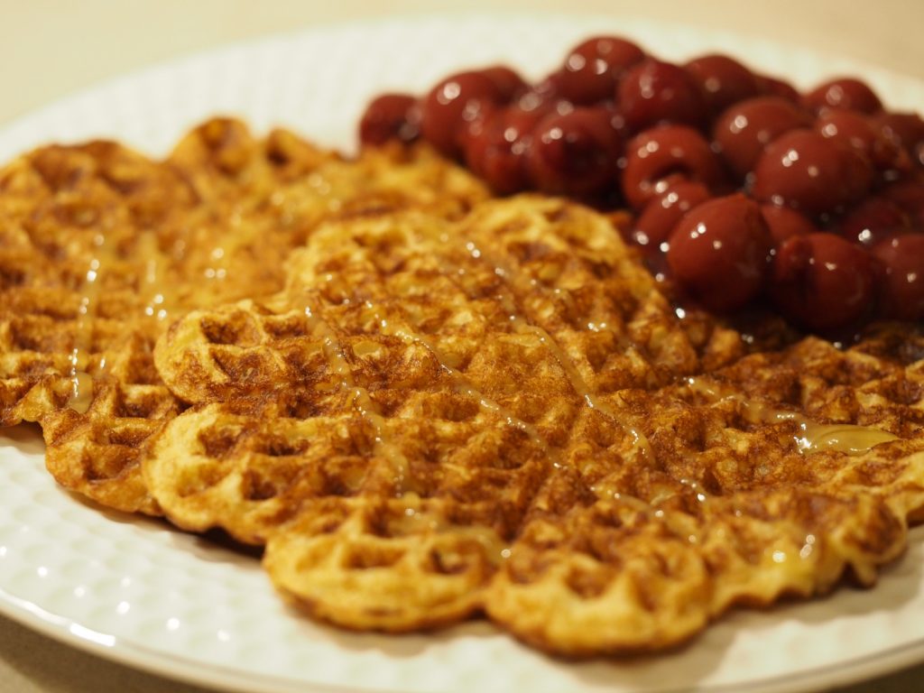 Zwei Waffeln auf einem großen Teller, daneben etwas Kirschkompott. Die Waffeln wurden mit etwas Honig beträufelt.