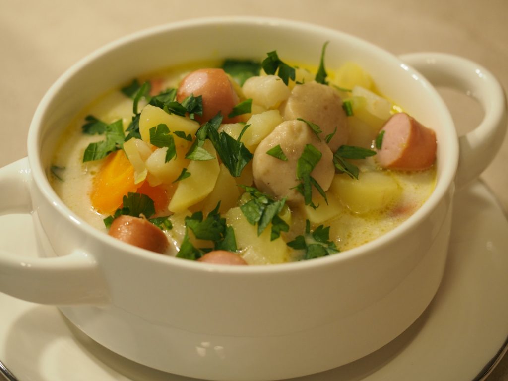 Eine kleine Suppenschüssel gefüllt mit der Kartoffelsuppe mit Würstchen und Markklößchen und etwas frischer Petersilie