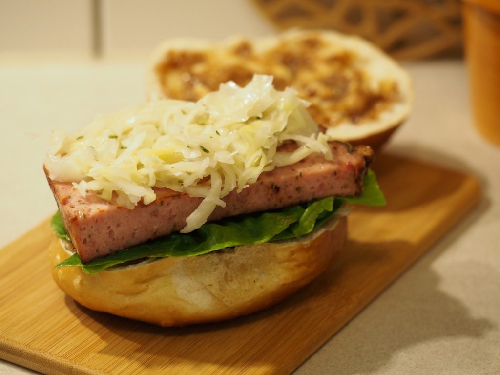 Der noch offene Leberkäswecken mit süßem Senf, Salat und Krautsalat im Laugenwecken.