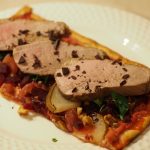 Ein großes Stück Flammkuchen gebacken mit roter Bete und Birne, belegt mit gebratener Entenbrust, gehackter Petersilie und bestreut mit etwas Zartbitter Schokolade