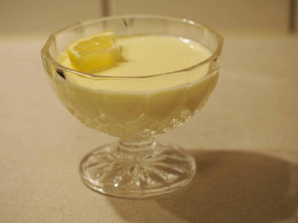 Ein Lemon Posset, eine britische Zitronencreme, in einer kleinen gläsernen Dessertschale, dekoriert mit einem Stück einer Zitronenscheibe