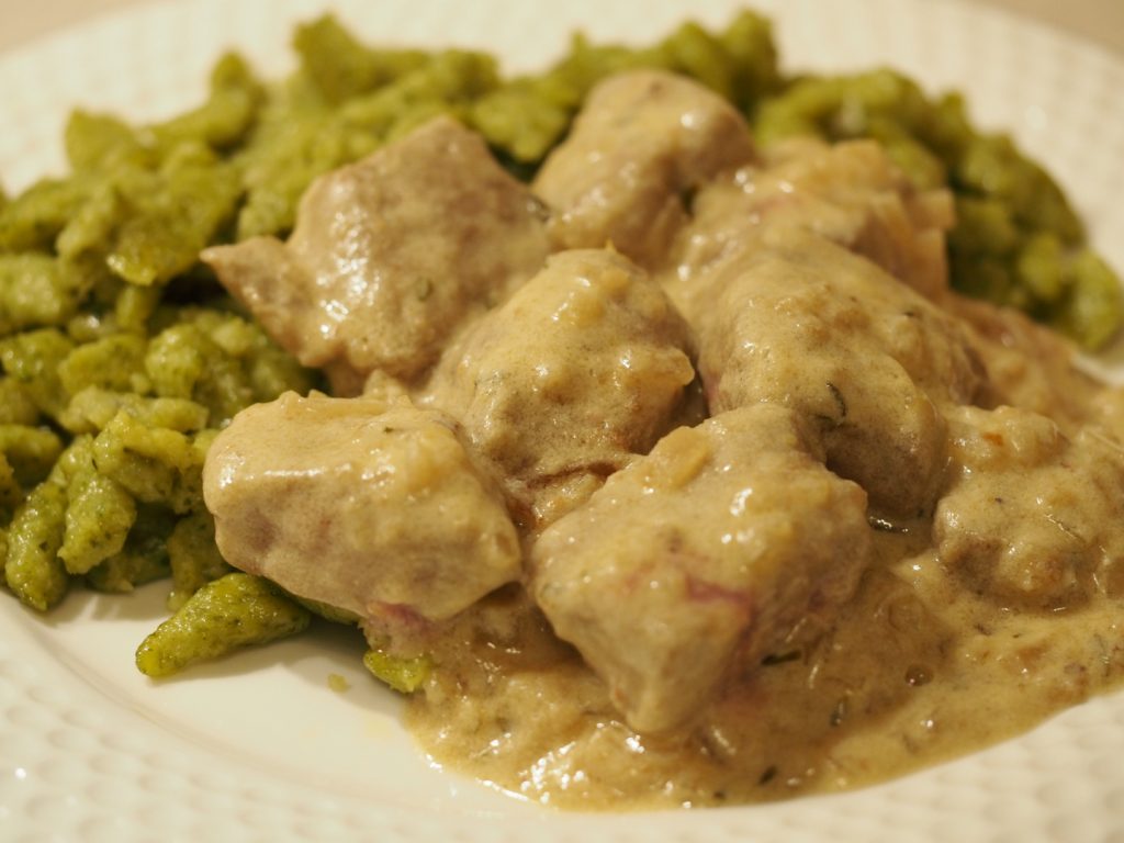 Kalbsleberstücke gebraten und gegart in einer sauren Sauce mit Weißwein und Sahne. Dahinter und darunter liegen gebratene Spinatspätzle.