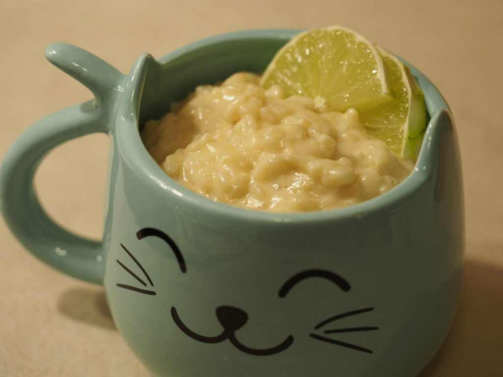 Eine Portion Milchreis, dekoriert mit zwei halben Scheiben Limette in einer türkisen Tasse mit Katzenohren