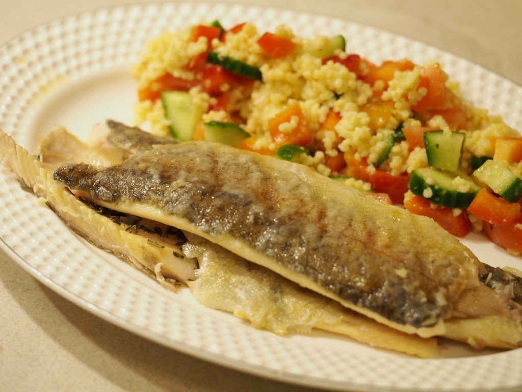 Die filetierte gebratene Forelle neben einer Portion Hirsesalat auf einem ovalen Teller