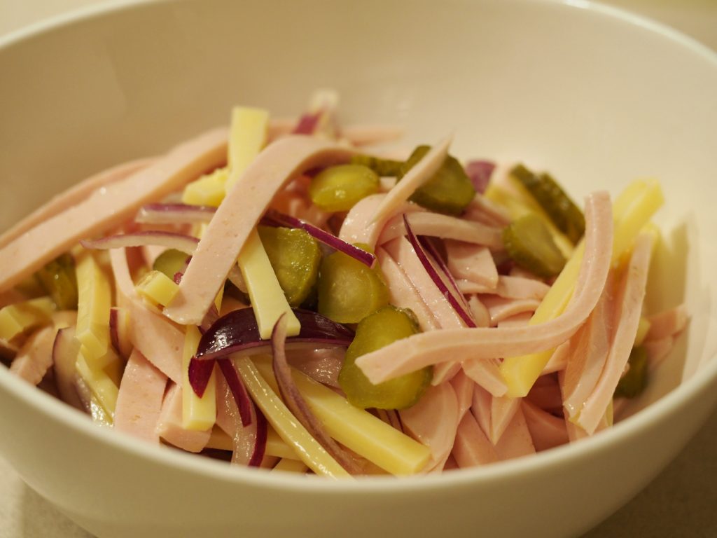 Eine Portion des Schweizer Wurstsalat mit Fleischwurst, Emmentaler, Cronichons und roter Zwiebel