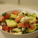 Eine kleine Schüssel gefüllt mit einem Salat aus rohen Zucchini, Tomaten, und Hirtenkäse