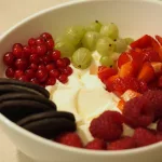 Eine Schüssel mit einer großen Portion Frozen Yogurt. Auf dem Dessert wurden rote Johannisbeeren, Stachelbeeren, Erdbeeren, Himbeeren und drei Oreo Kekse platziert.