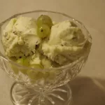 Eine kleine gläserne Dessertschale, gefüllt mit der Stachelbeeren-Eiscreme. Die Eiscreme wurde mit aufgetauten Stachelbeeren dekorieert.