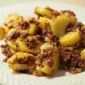 Eine Portion des Gröstl aus Blut- und Leberwurst und Kartoffeln auf einem weißen Teiller