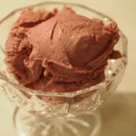 Eine gläserne Dessertschalte mit drei unförmigen Kugeln einer Kirsch-Eiscreme