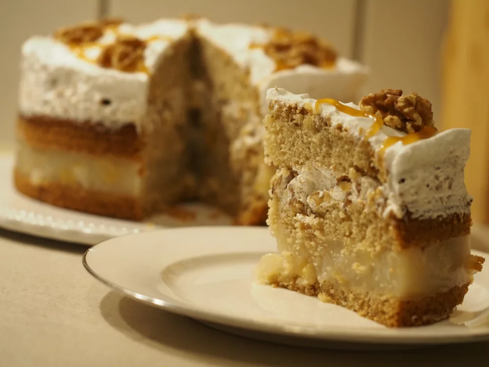 Die angeschnittene Torte im Hintergrund. Ein einzelnes Stück auf einem weißen Kuchenteller im Vordergrund.
