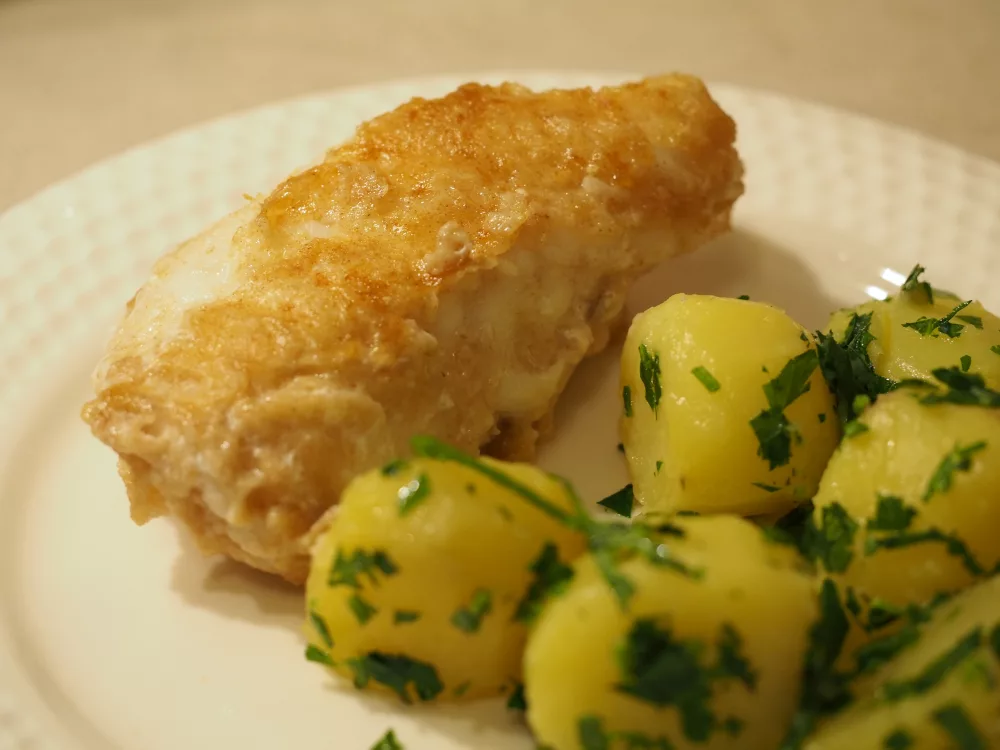 Ein Stück mehliertes und gebratenes Seeteufelfilet neben ein paar Petersilienkartoffeln