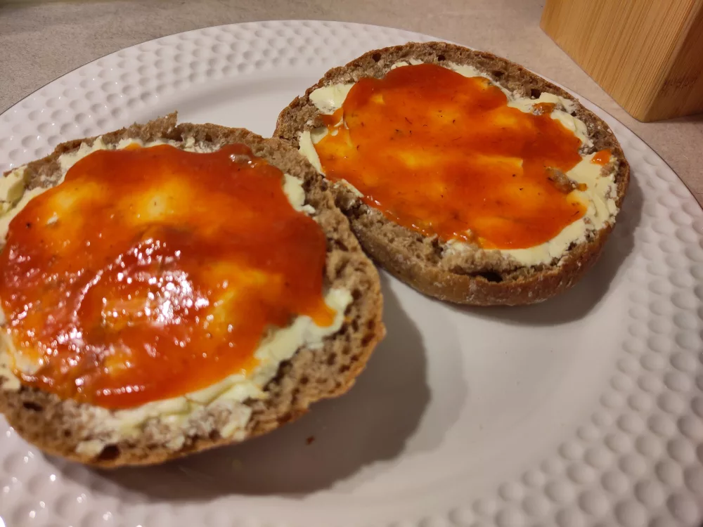 Auf einer dunklen Semmel wurde auf etwas Margarine jeweils etwas von der rot-orange farbenen Marmelade verteilt.
