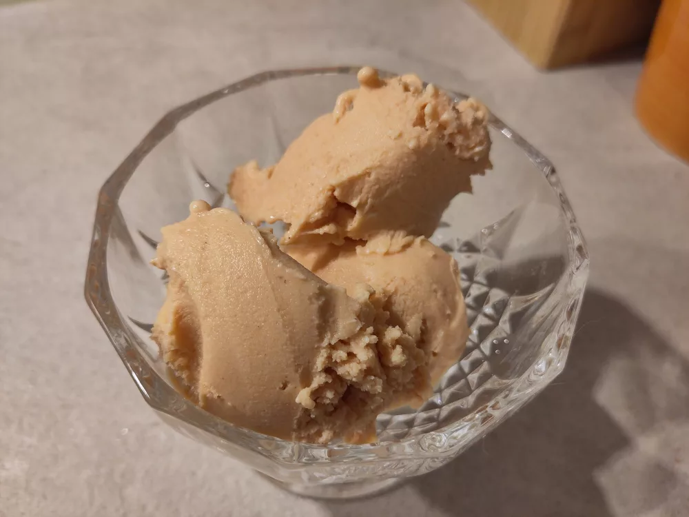 Drei unförmige Kugeln der Hagebutten-Birnen Eiscreme in einer gläsernen Dessertschale