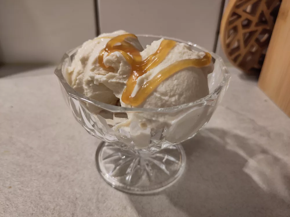 Eine gläserne Dessertschale gefüllt mit drei Kugeln Karamelleiscreme, welche mit noch etwas zusätzlicher Karamellsauce besprenkelt wurden.
