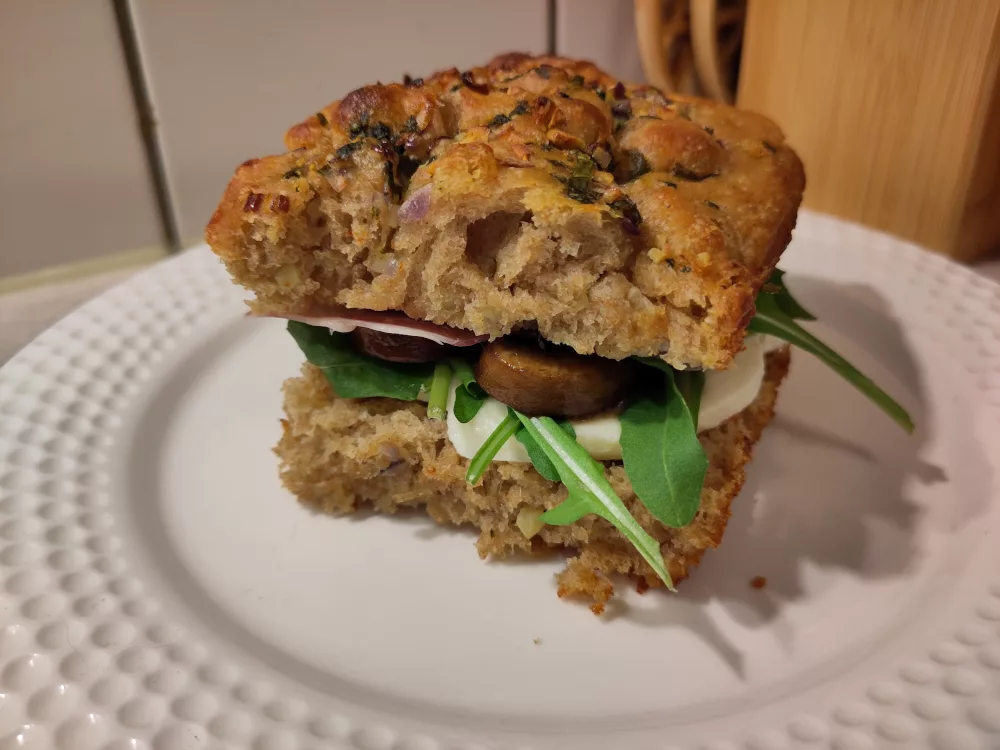 Das fertige Sandwich auf einem weißen Teller. Am Rand sind man jeweils etwas von dem Mozzarella, Rucola, den Pilzen und dem Schinken