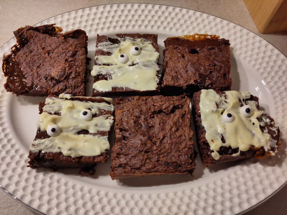 Sechs Stücke des Süßkartoffel-Brownie auf einer Servierplatte. Drei der Stücke wurden mit weißer Schokolade und Zuckeraugen, passend für Halloween dekoriert.