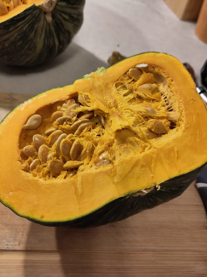 Der halbierte Kürbis gibt den Blick auf das gelbe Fruchtfleisch und die Kerne im Inneren frei.