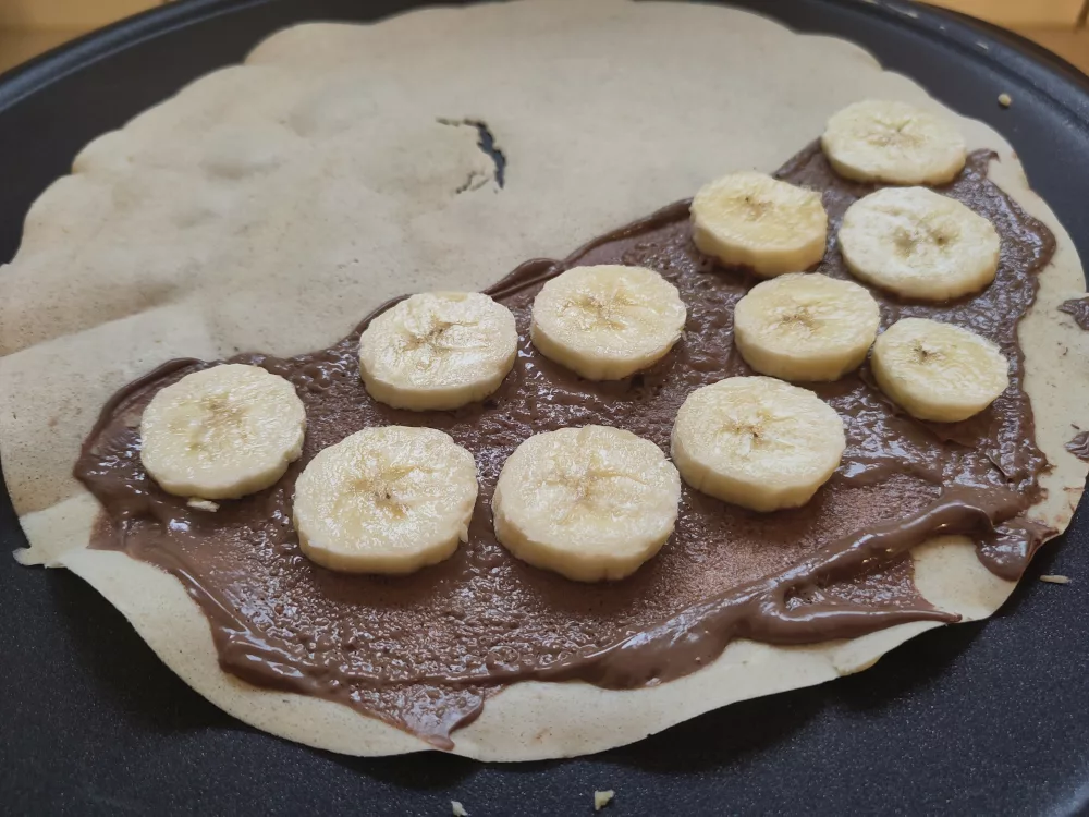 Ein Crepe wurde gewendet und auf der unteren Hälfte mit Nougatcreme bestrichen und mit Bananenscheiben belegt.