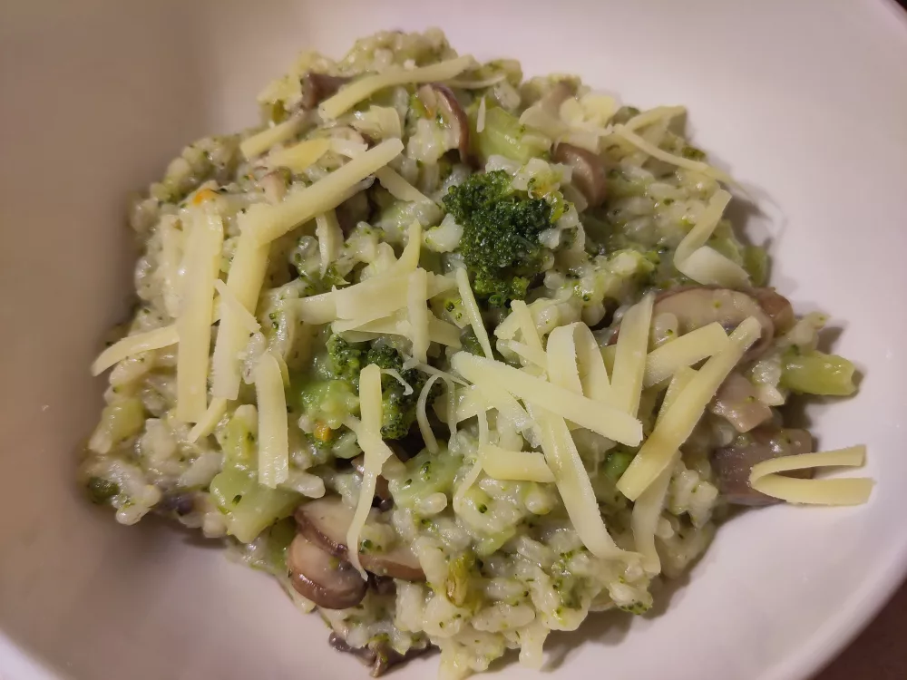 Eine Portion des Risotto mit Brokkoli und Champignons. Die Portion wurde mit etwas gehobelten Bergkäse bestreut.
