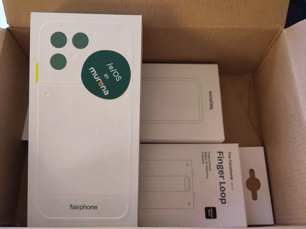 Ein noch verpacktes Fairphone 6 mit murena Betriebssystem und ein paar Zubehörsachen ebenfalls verpackt wie beispielsweise eine passende Hülle, eine Fingerschlaufe, etc.
