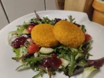 Zwei gebackene Camembert auf einem Salat auf dem noch ein paar Kleckse Preiselbeeren verteilt wurden