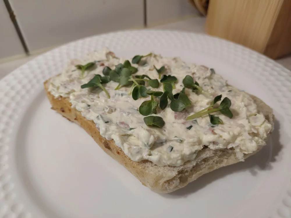 Ein aufgeschnittenes Brötchen das großzügig mit der Forellencreme bestrichen wurde. Der Belag wurde mit Radieschensprossen dekoriert.