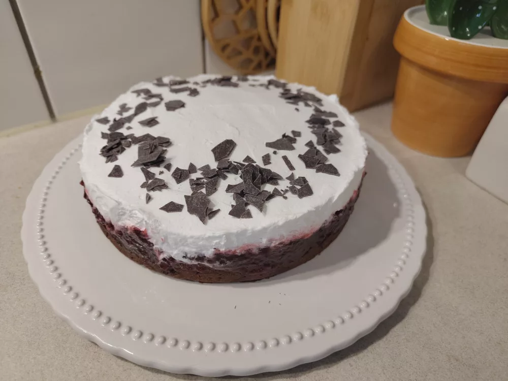 Ein Schokoladenkuchen wurde mit Preiselbeeren und aufgeschlagener veganer Sahne bestrichen und mit Schokoladensplittern dekoriert.