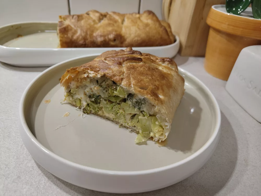 Ein Stück des Brokkoli Strudel auf einem Teller im Vordergrund. Dahinter der angeschnittene Strudel von dem nun ein Viertel fehlt.
