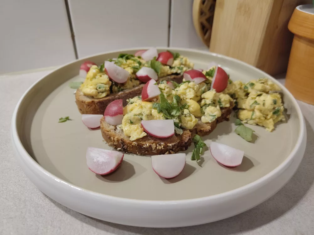 Zwei Brotscheiben wurden üppig mit dem Rührei und Radieschen-Viertel belegt. Drum herum sind noch weitere Radieschen-Stücke und ein Rest Rührei.