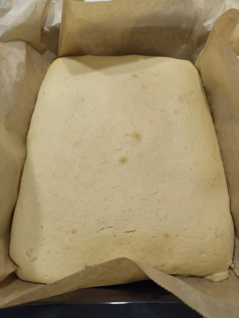 der halbgebackene Kuchenteig in einer eckigen Backform, die mit Backpapier ausgekleidet ist.