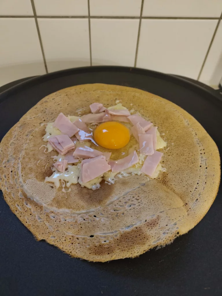 Auf eine Galette wurden im Zentrum geriebener Käse, Schinken und in der Mitte ein Ei gegeben.