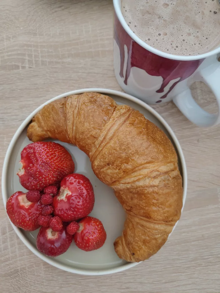Frische Erdbeeren mit einem Croissant auf einem Teller, daneben eine große Tasse Chai