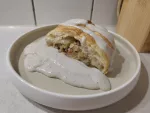 Ein Stück des Rhabarber-Strudels auf einem Teller, mit einer großzügigen Portion Vanillesauce