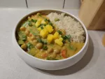 Eine Portion des Currys mit Kichererbsen, Kaiserschoten und Mango, daneben etwas gekochter Reis