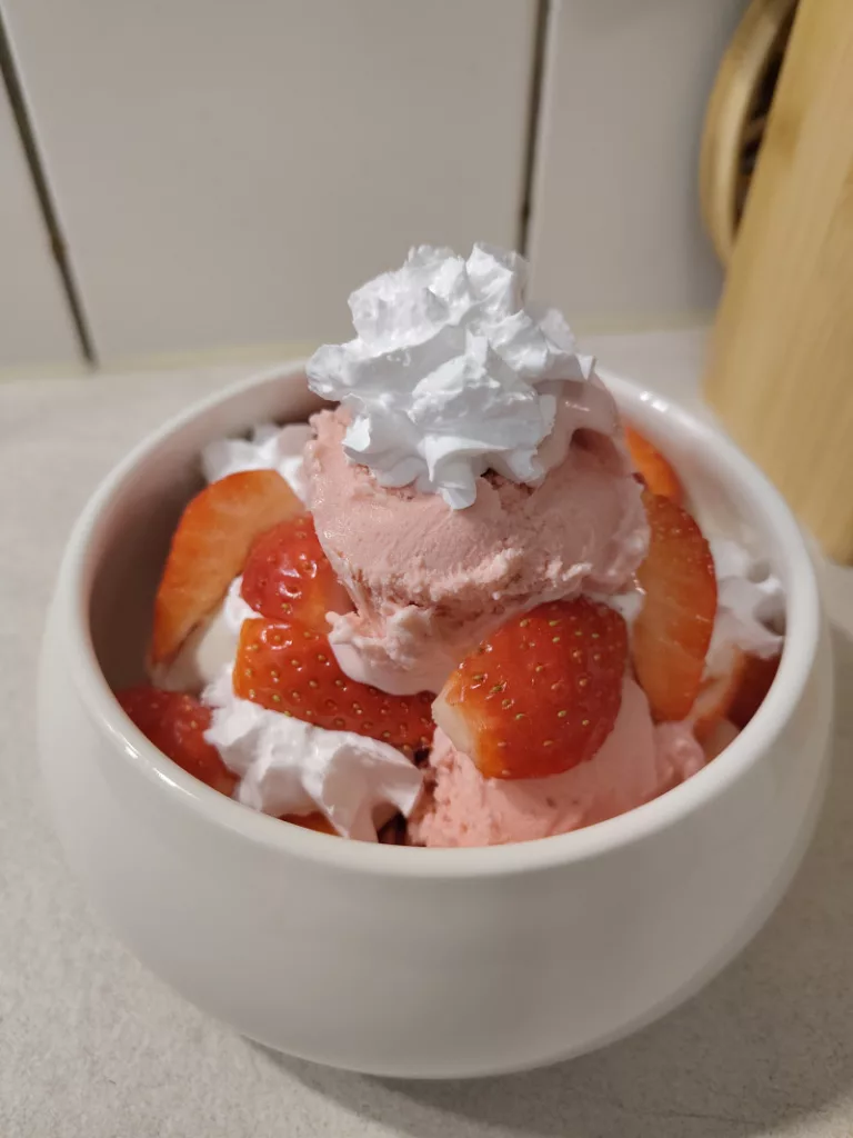 Ein gut gefülltes Schüsselchen mit Erdbeer-, Vanilleeiscreme, vegane Sahne und frischen Erdbeeren.