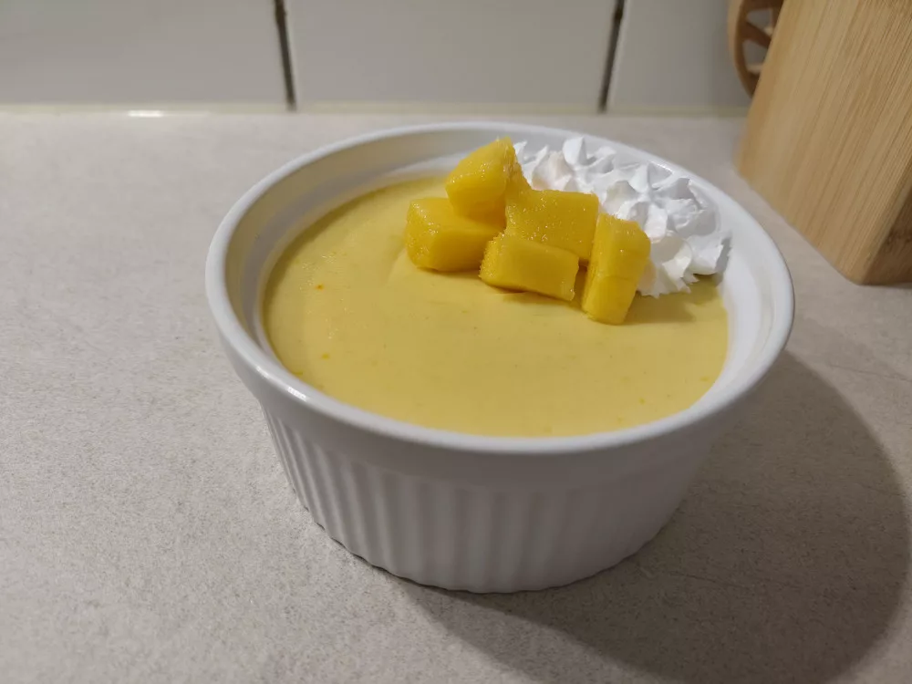 Ein Schälchen mit der Mango-Ricotta Creme, garniert mit frischen Mango-Würfeln und ein paar Tupfen vegane Sahne.