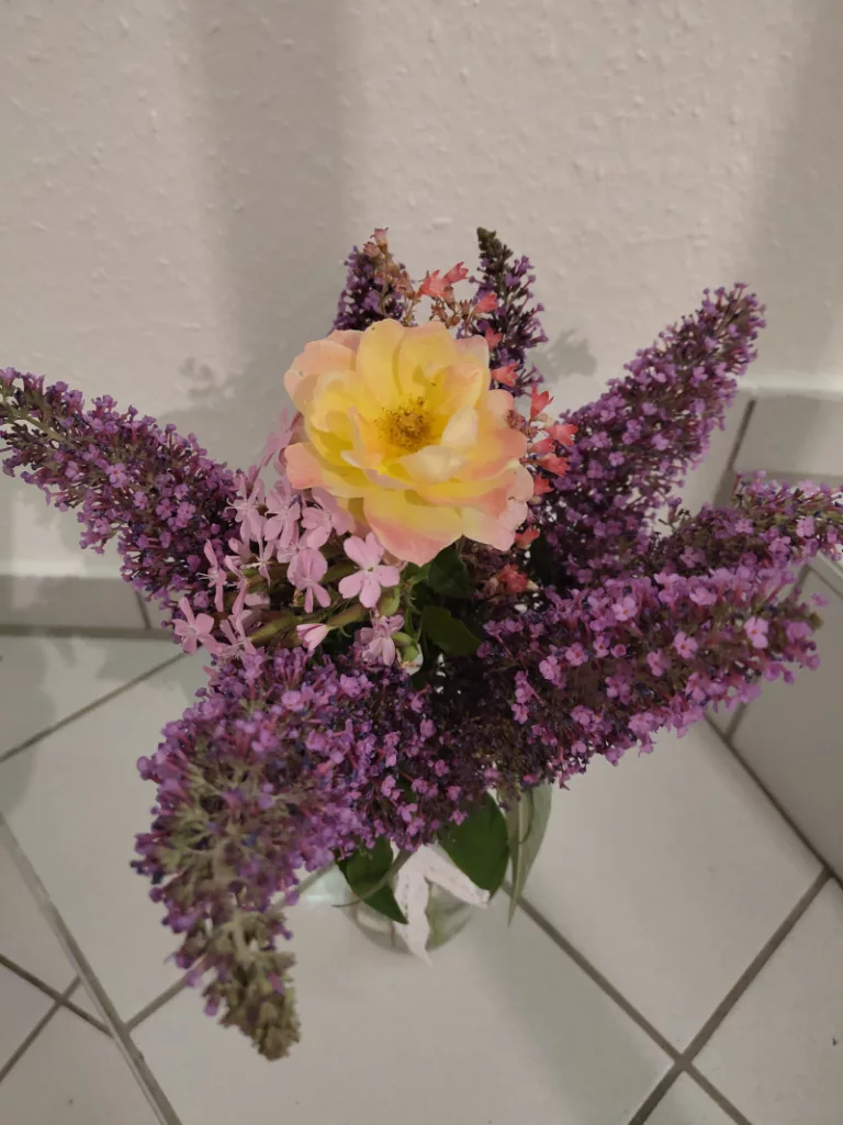 Ein Blumenstrauß aus Sommerflieder, Seifenblume, Porzellanblümchen und einer gelb-orangenen Rose steht auf der Kellertreppe bereit um ihn für einen Besuch mitzunehmen.